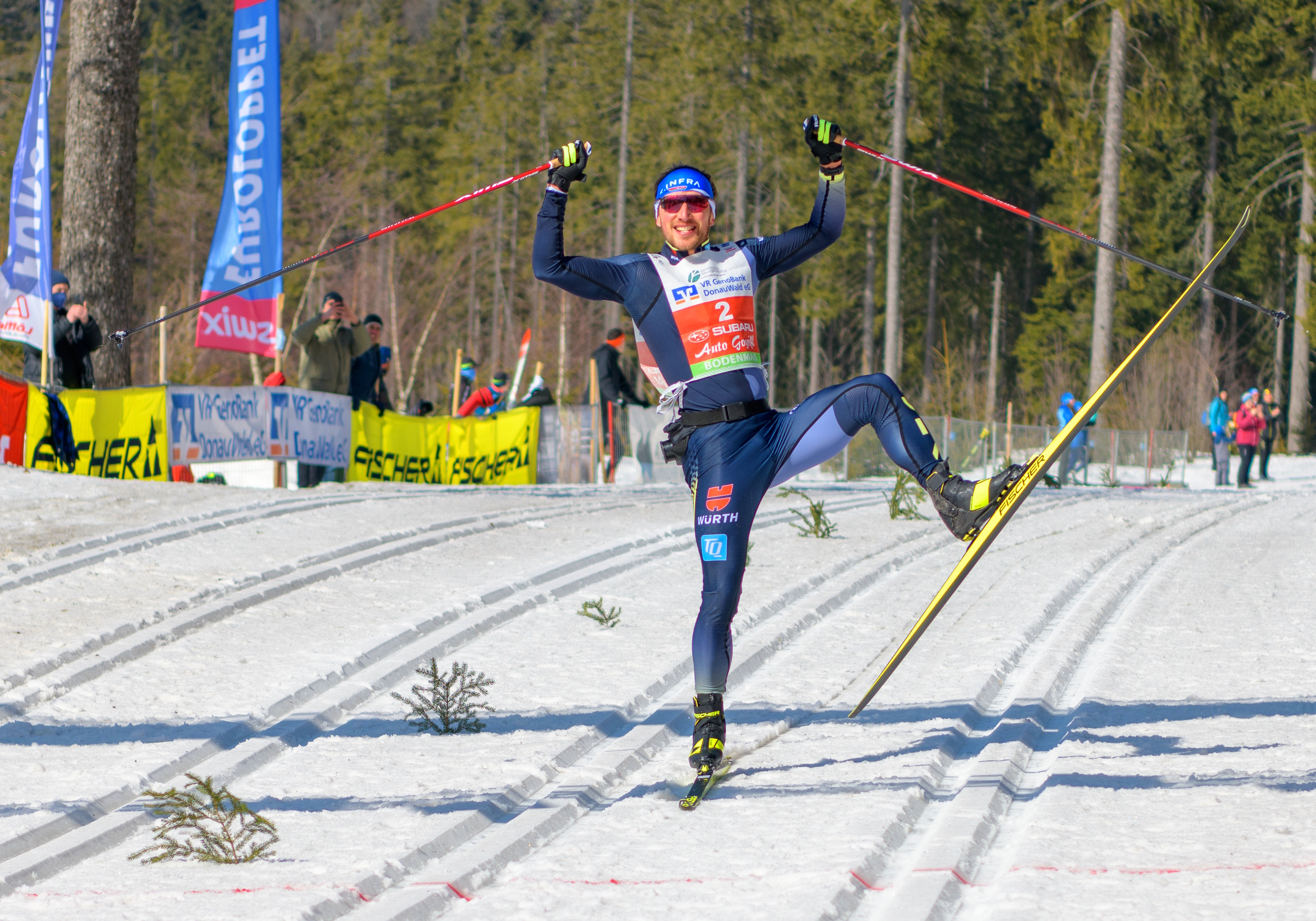 Skimarathonläufer freut sich bei der Zieleinfahrt und fährt nur auf einem Ski und reißt die Arme nach oben und lächelt