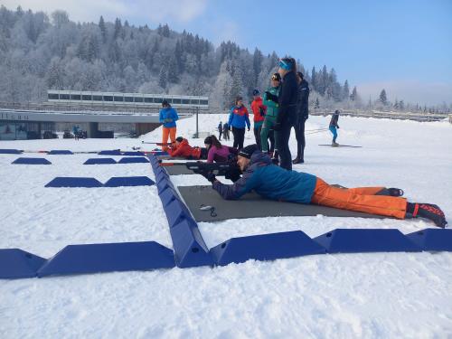 Personen stehen und liegen an einer Biathlonschießanlage und schießen mit einem Biathlongewehr